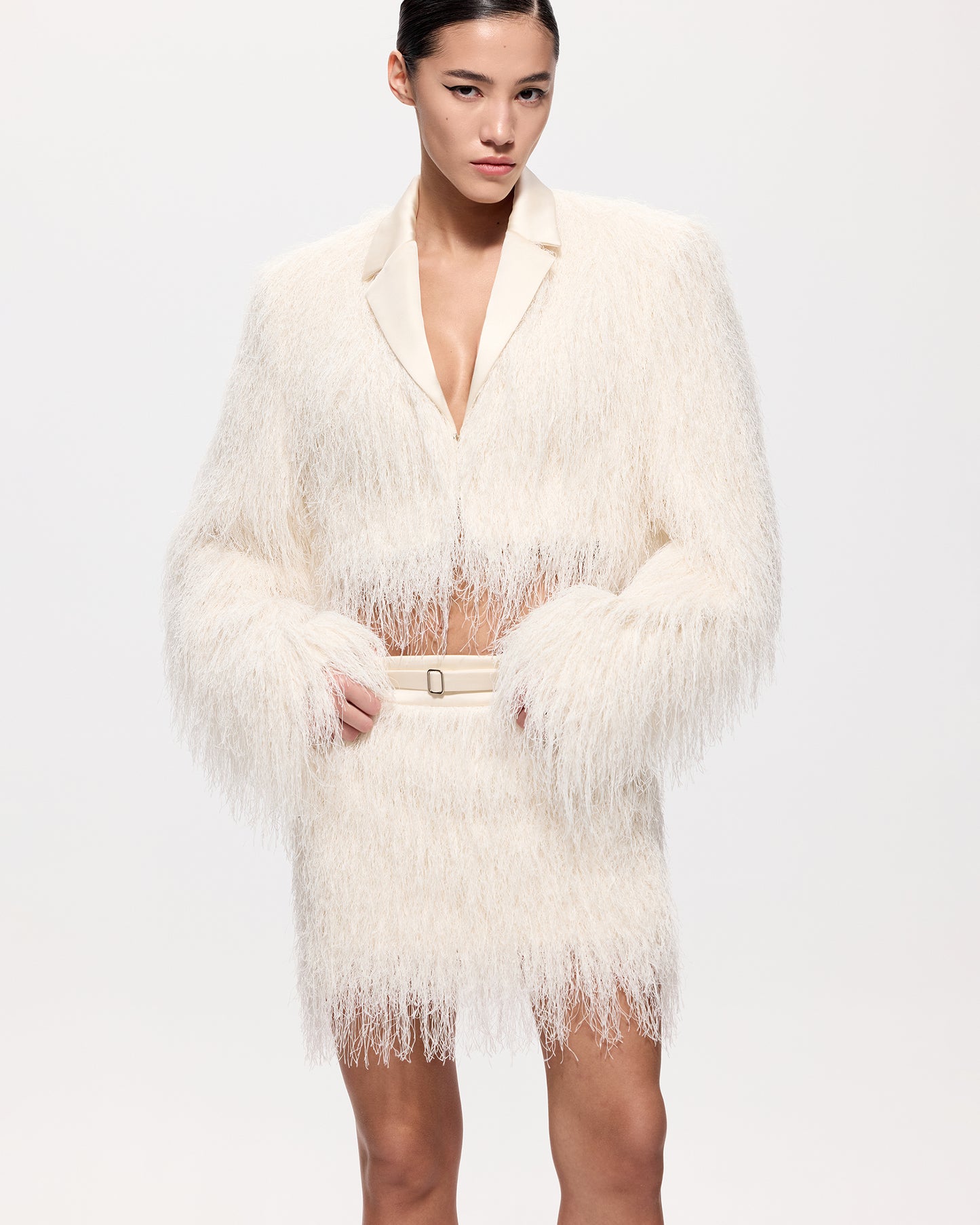 Woman wearing a white feathered coat and skirt on a plain background